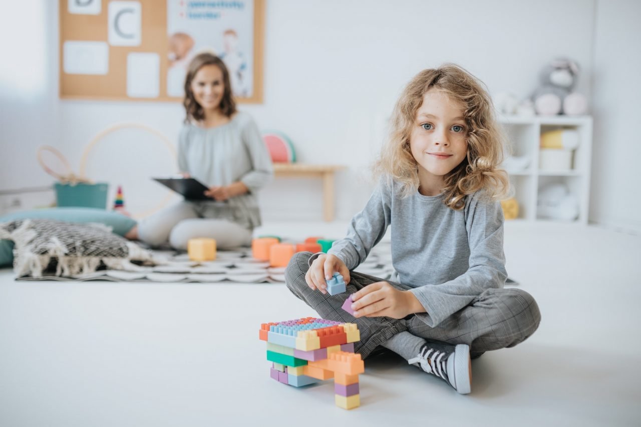 Niña en una sesión terapéutica con psicólogo infantil, participando activamente en un ambiente de apoyo emocional mirando a la cámara para retrato.
