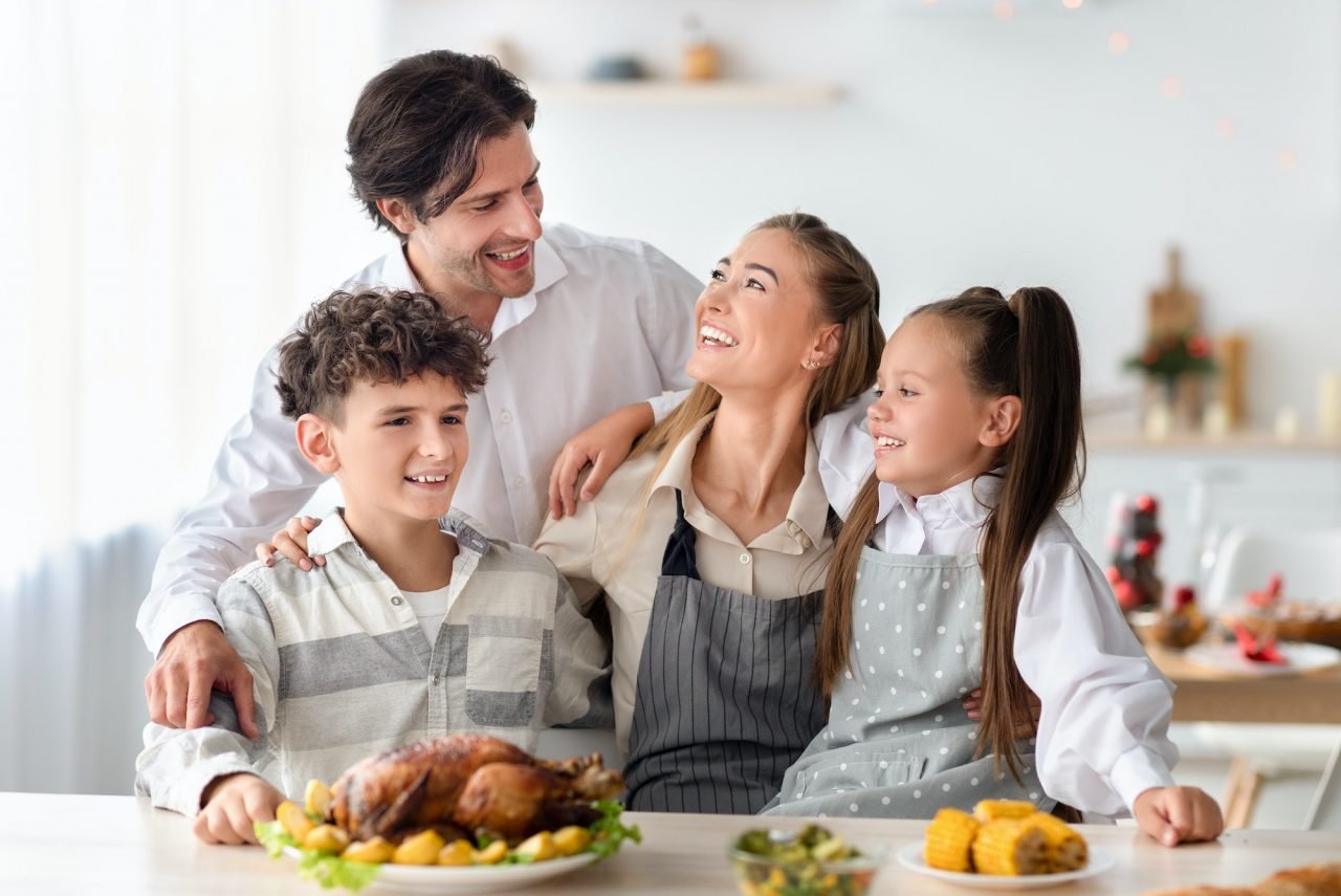 Familia feliz, padres e hijos en la cocina preparando una comida navideña, compartiendo momentos de alegría y unión familiar.