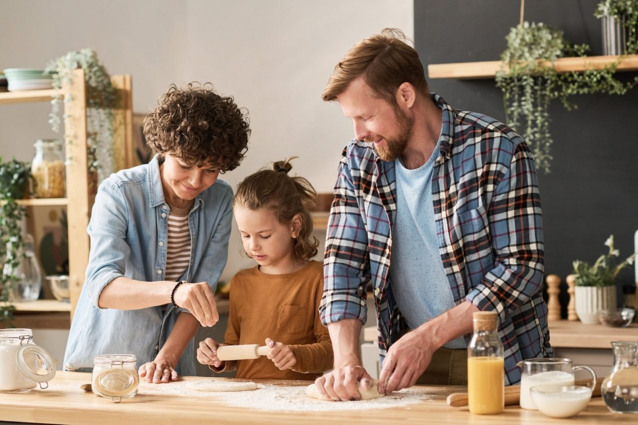 Padres enseñando a su hijo a preparar una tarta en la cocina, compartiendo una actividad familiar divertida y educativa.